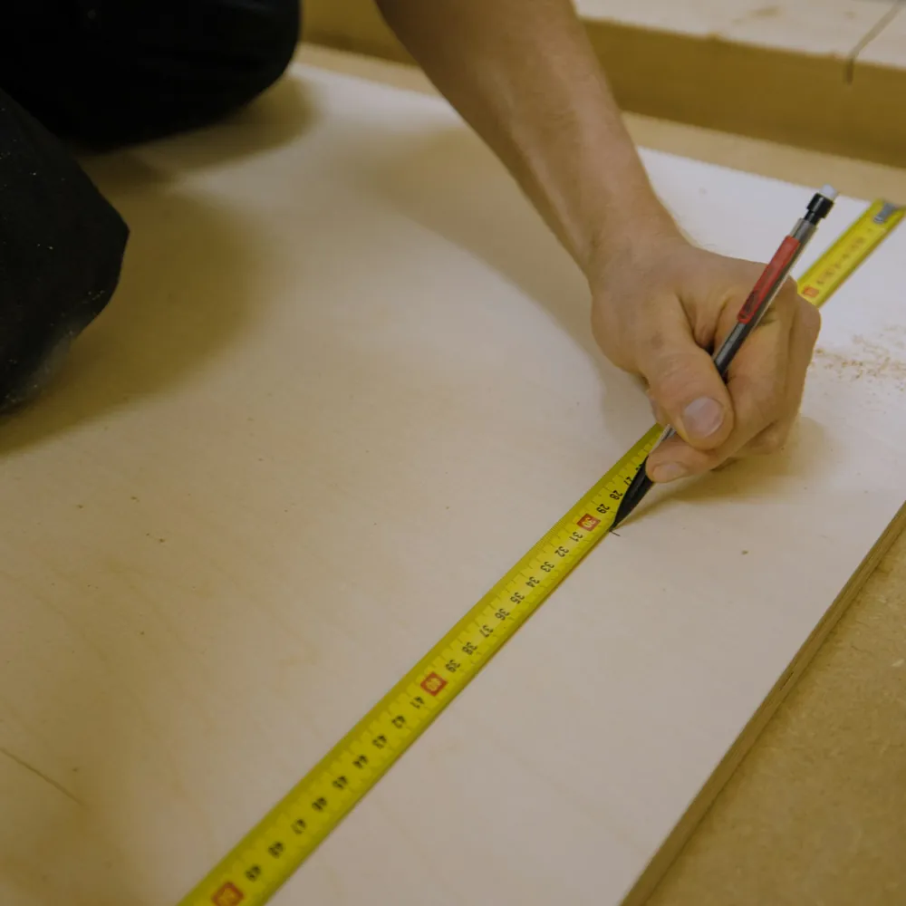 Manos midiendo un listón de madera sobre el banco de un taller de enmarcado